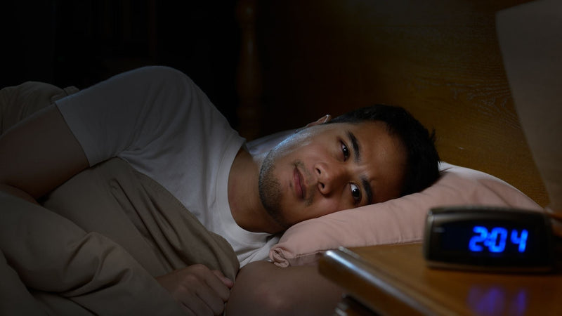 Man lying awake with insomnia staring at the clock at 2 AM