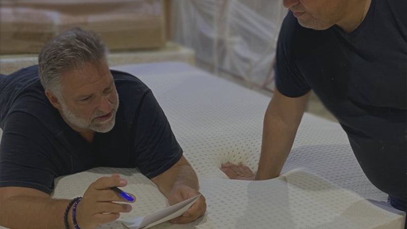 Jack Dell'Accio, Founder & CEO of Essentia, lying down on some latex in the factory explaining something to a craftsman